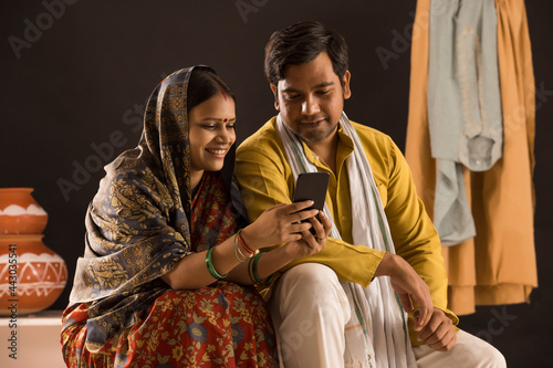 A RURAL WIFE AND HUSBAND SITTING TOGETHER AND USING MOBILE PHONE