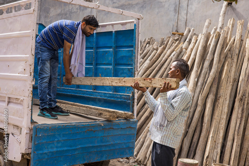 TWO WORKERS UNLOADING A TRUCK WITH WOODEN POLES photo