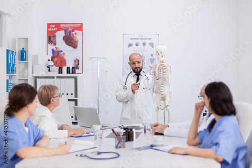 Physician doctor with stethoscope holding hand bone explaining body human skeleton presenting anatomy structure discussing medical expertise. Hospital team working in conference meeting room