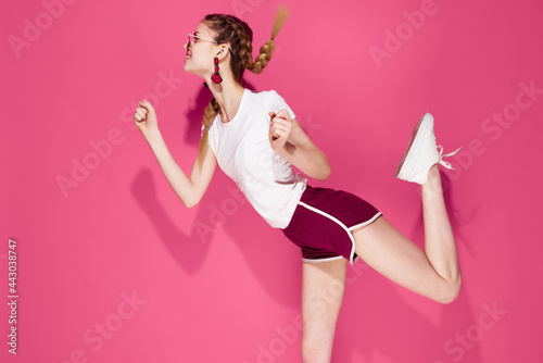 pretty sportive woman in bent leg on pink background wearing glasses © SHOTPRIME STUDIO