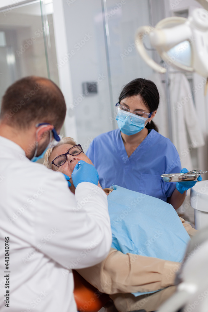 Obraz premium Dentist with assistant install implant in patient mouthin modern clinic. Elderly woman during medical examination with stomatolog in dental office with orange equipment.