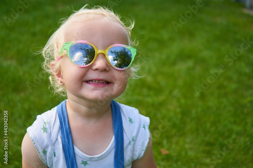 laughing little girl in sunglasses,beautiful happy little girl laughs in sunglasses on a background of grass