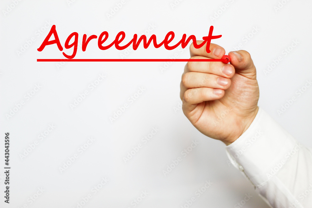A businessman in a white shirt writes a text AGREEMENT on a white background with a red marker . business concept A businessman in a white shirt writes a text AGREEMENT on a white background with a red marker . business concept