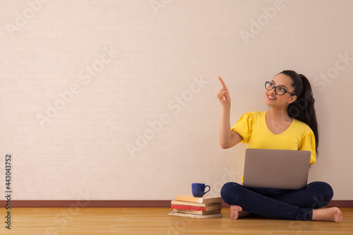 A young woman pointing elsewhere while working on laptop.