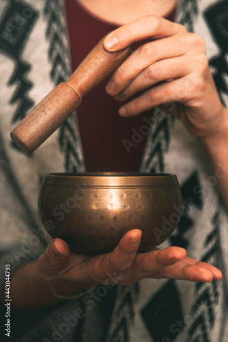hands of a woman using a golden tibetan bowl in a meditation dressed with a handmade poncho. background with copy space. concept meditation. vertical image