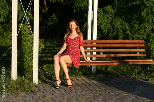 Beautiful slender woman ir red dress sitting on a bench in park