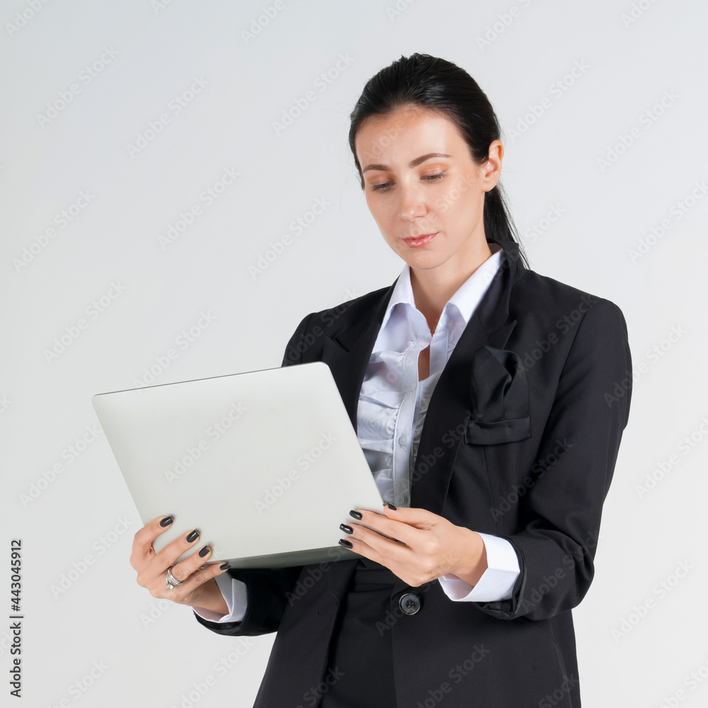 Young caucasian business woman in black suit looking at laptop computer screen on her hand. Portrait on white background with studio light. Young caucasian business woman in black suit looking at laptop computer screen on her hand. Portrait on white background with studio light.