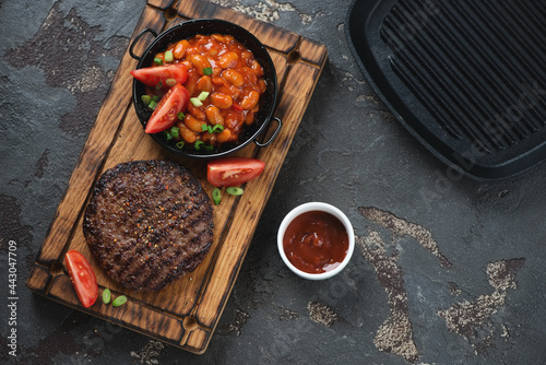 Rustic wooden serving tray with grilled balkan meat patty or pljeskavica and prebranac, above view on a brown stone background with copyspace photo