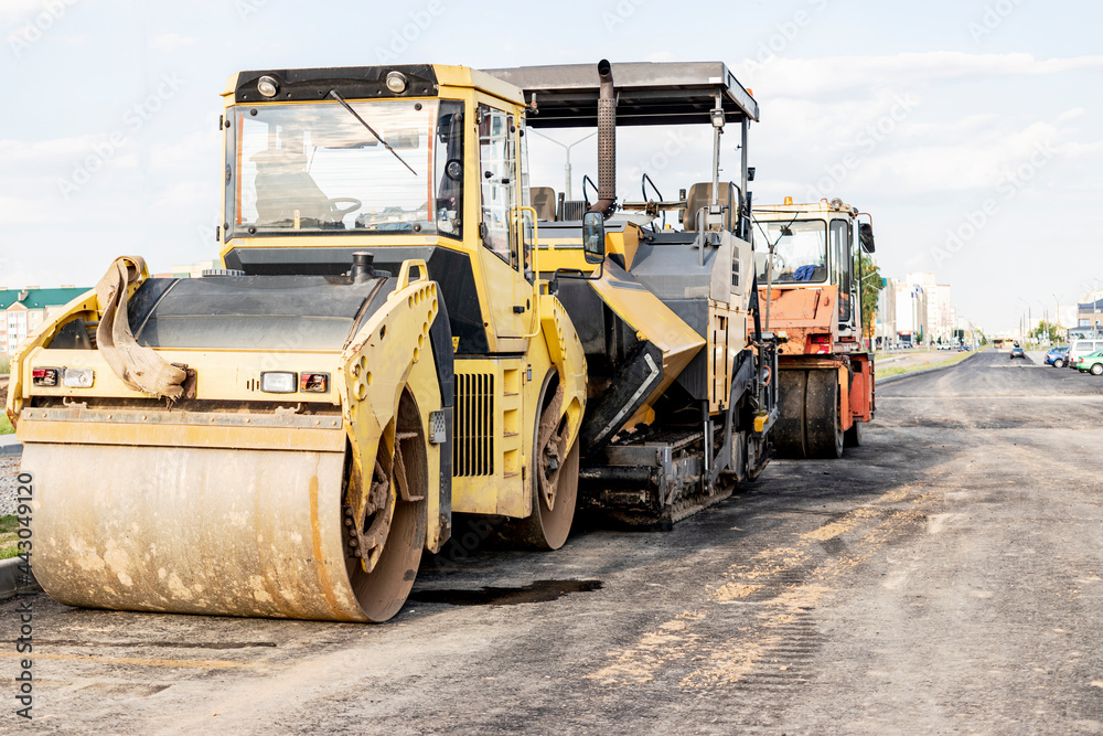 Asphalt paving equipment. Asphalt paver and heavy vibratory roller. Construction of new roads and road junctions. Heavy construction industrial machinery. Asphalt paving equipment. Asphalt paver and heavy vibratory roller. Construction of new roads and road junctions. Heavy construction industrial machinery.