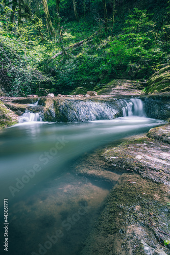 Scenic look on rapids of the waterfall in the Dzykhrinskoye gorge with lush green and trees behind. Water basin and rocks at the foot of the waterfall. Travel  hiking Adler microdistrict  Russia.