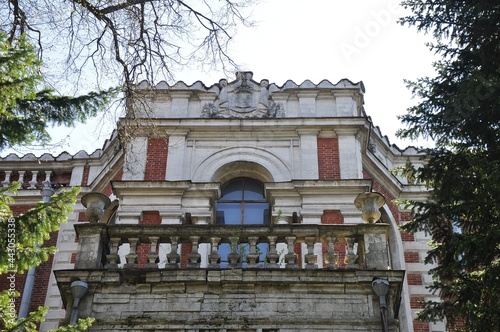The overgrown and abandoned facade of the manor house of a noble estate made of red bricks with white trim. The main house of the Bykovo estate.