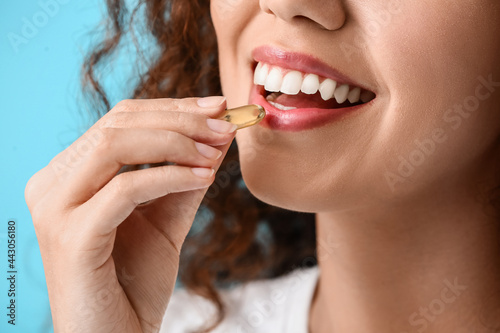 Young woman taking fish oil pill on color background