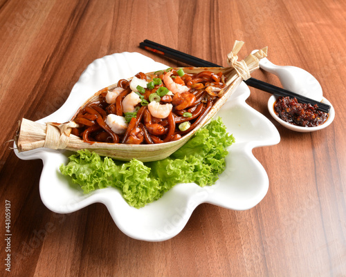 stir fried hokkien dark soy sauce udon noodle with seafood and meat in leaf on wood table asian halal menu photo