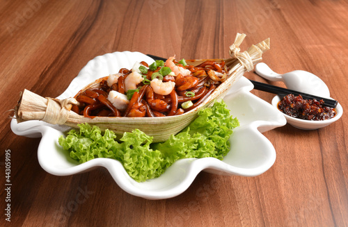 stir fried hokkien dark soy sauce udon noodle with seafood and meat in leaf on wood table asian halal menu photo