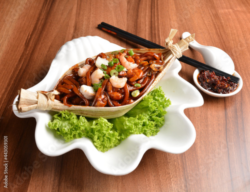 stir fried hokkien dark soy sauce udon noodle with seafood and meat in leaf on wood table asian halal menu photo