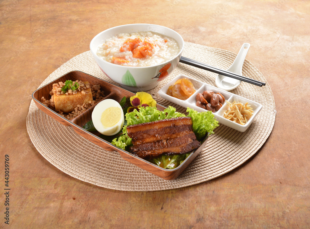 double boiled pumpkin rice congee porridge with braised pork belly , egg, fried bean curd tofu and peanut sour vegetable bento set on wood table asian halal menu