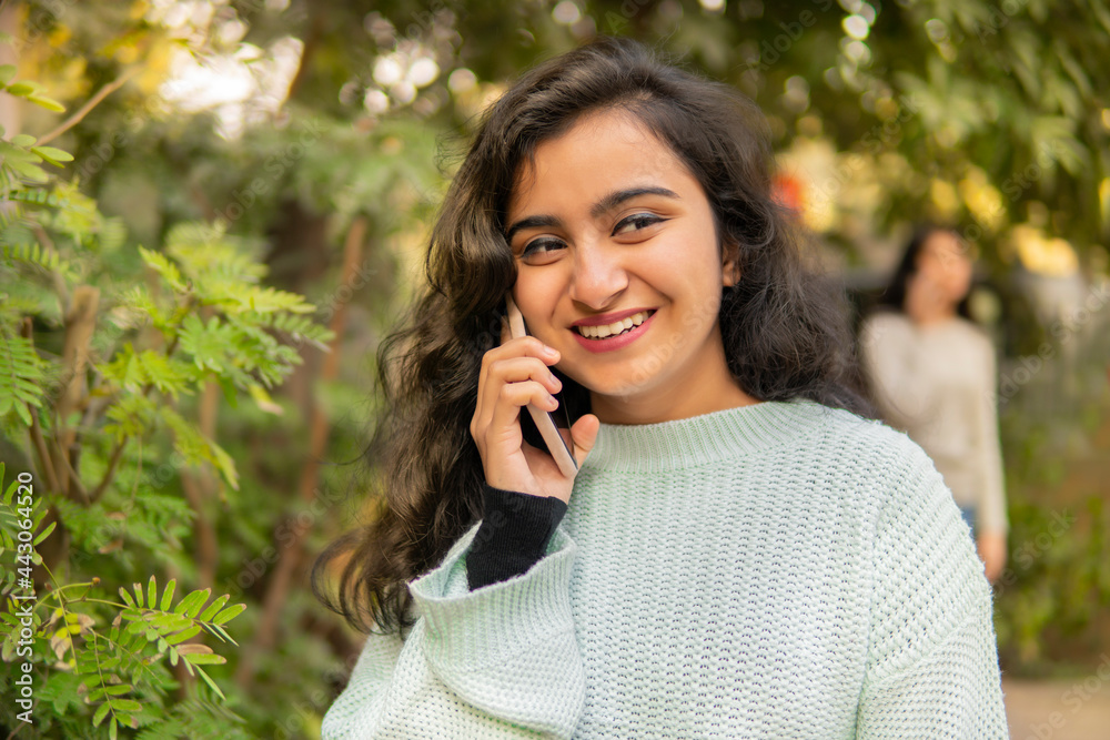 Outdoor image of an Asian, Indian beautiful happy young woman talking on smartphone in park and enjoying the fresh air at day time. Outdoor image of an Asian, Indian beautiful happy young woman talking on smartphone in park and enjoying the fresh air at day time.