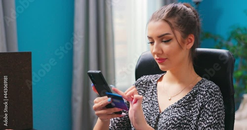 Gorgeous young girl sititng at home using mobile banking application on her gadget while paying bills using free internet connection. Busy woman sitting at living room with credit card and phone photo