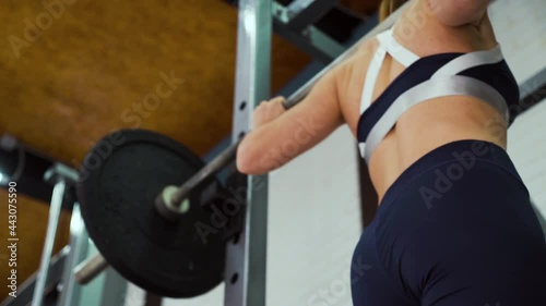 Young strong woman in sportswear squatting with barbell. Low angle female bodybuilder working out in gym. Concept of sport