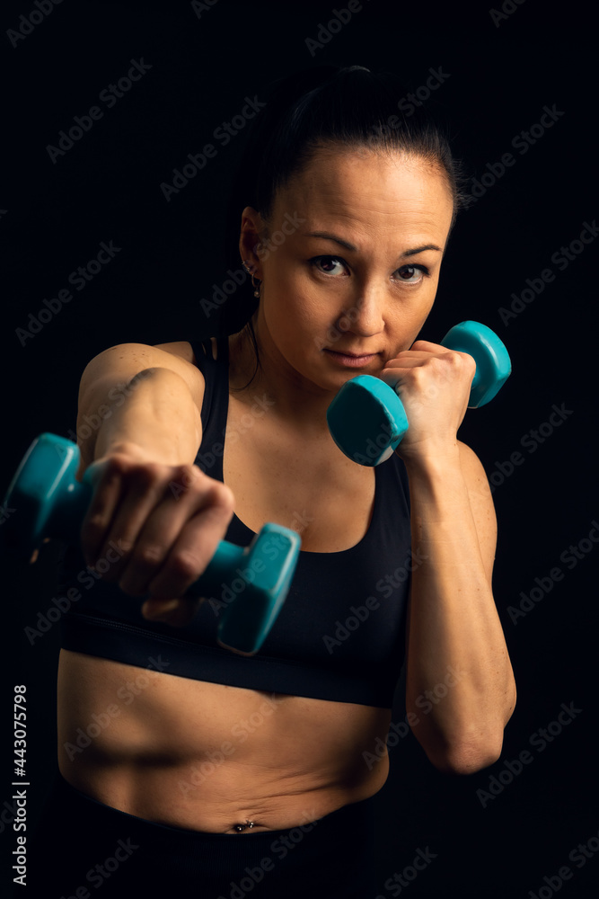 Vertical portrait, in studio, in front of a black background, of an Asian fighting athlete, Korean, boxing with weights in her hand, looking at the camera, with a serious, determined expression. Vertical portrait, in studio, in front of a black background, of an Asian fighting athlete, Korean, boxing with weights in her hand, looking at the camera, with a serious, determined expression.