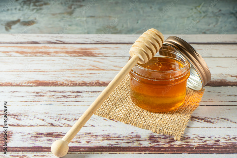 Jar of pure honey from bees with the wooden honey stick resting on the jar on a rustic table. Jar of pure honey from bees with the wooden honey stick resting on the jar on a rustic table.