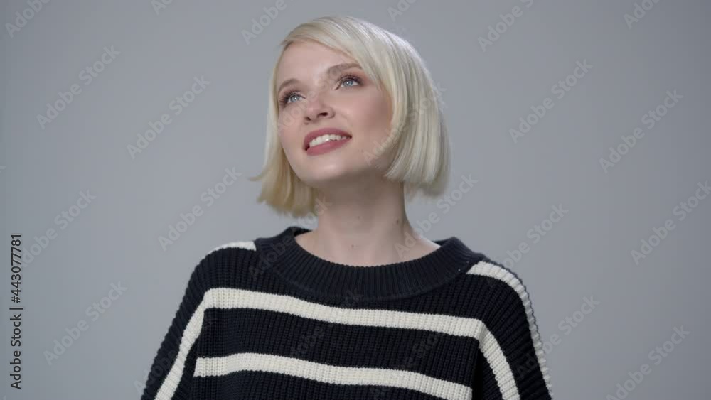Attractive blonde with short hairstyle is having fun and posing for the camera. Gray background. Attractive blonde with short hairstyle is having fun and posing for the camera. Gray background.