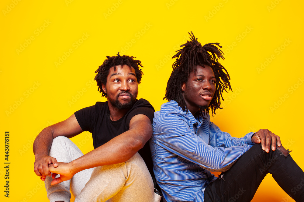 Obraz premium two african american guys posing cheerful together on yellow background, lifestyle people concept