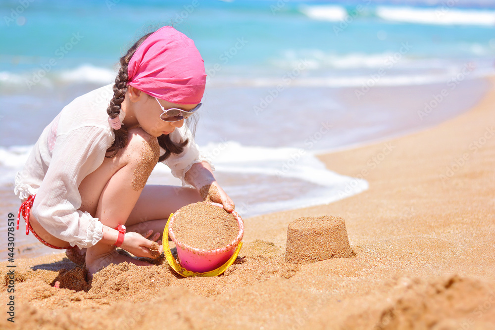 A beautiful little girl builds sand towers on the beach near the sea. Family beach leisure and vacation concept A beautiful little girl builds sand towers on the beach near the sea. Family beach leisure and vacation concept