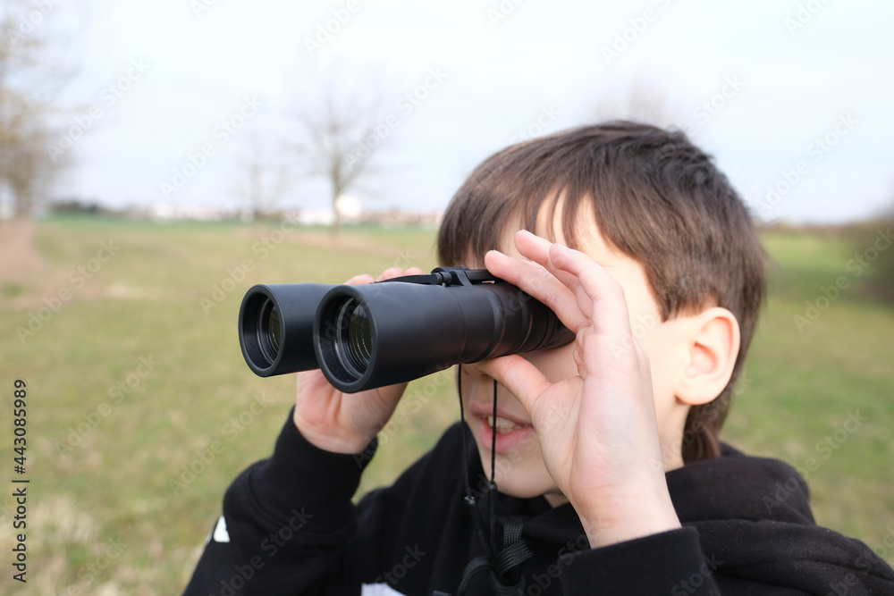 boy, guy 8-10 years old stalker looks through black binoculars in the park, spies, hunts down secrets, the concept of surveillance, observation of people and animals boy, guy 8-10 years old stalker looks through black binoculars in the park, spies, hunts down secrets, the concept of surveillance, observation of people and animals