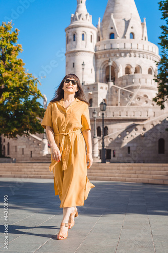 Solo traveler woman portrait. Stylish fashionable happy middle aged woman traveler wearing yellow dress walks in Fisherman Bastion in Budapest Hungary. © Inna