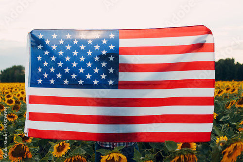 Young woman with American flag in the sunflower field. 4th of July Independence Day USA concept