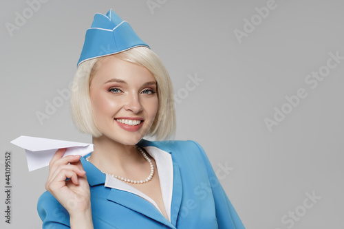 Attractive blonde flight attendant launches a paper airplane. Gray background. photo