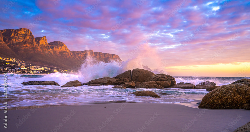 Naklejka premium Beautiful sunset as waves crash on the rocks at Maiden's Cove beach, Camps Bay. The Twelve Apostles Mountain Range is where you'll find one of most scenic stretches of coast in the world