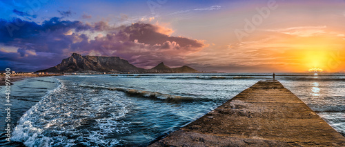 Picturesque and colourful sunset scene of Table Mountain and The Atlantic Ocean. A jetty reaches out to the cool blue sea to inspire a sense of adventure. A stunning tourist destination - Cape Town