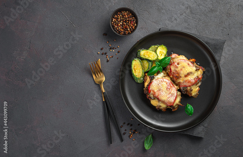 A portion of baked meat with cheese and mushrooms in a black plate on a dark background. Meat dish with vegetables.