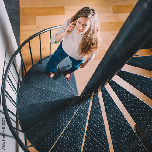 Pretty young girl climbing up the round staircase, holding cell phone and looking at the camera