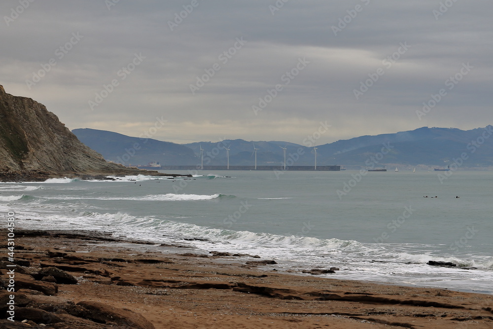 Rocas en playa de Azkorri, Getxo, Bizkaia, España. Foto de las rocas y olas con los molinos del puerto de fondo.