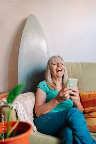 Elder woman using smartphone and laughing out loud while sitting on sofa at home photo