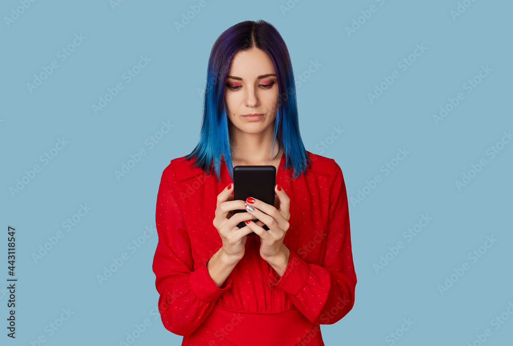 Happy young woman in red dress and sunglasses with blue hair holding smartphone Happy young woman in red dress and sunglasses with blue hair holding smartphone