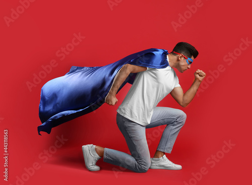 Man wearing superhero cape and mask on red background