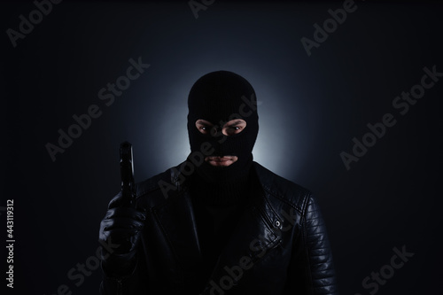 Fototapeta Naklejka Na Ścianę i Meble -  Man wearing knitted balaclava with gun on black background