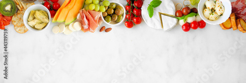 Italian theme charcuterie top border against a white marble banner background. Assortment of cheese, meat and fruit appetizers. Above view with copy space.