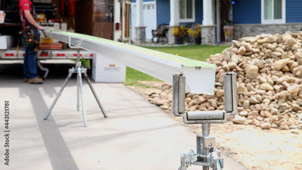 The end of a long aluminum rain gutter extends out to a stand that keeps it straight, after it has been formed or shaped and extruded by a machine.