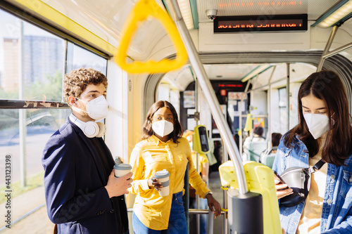 Men, women people passengers in masks riding inside public transport during coronavirus pandemic. Persons standing holding handles in bus or subway train. Social distancing concept.