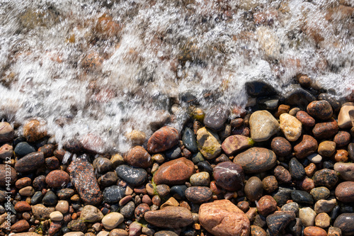 on the shores of the Baltic Sea there are stones of different colors, which form a beautiful pattern, where part of the image is covered by a foaming wave