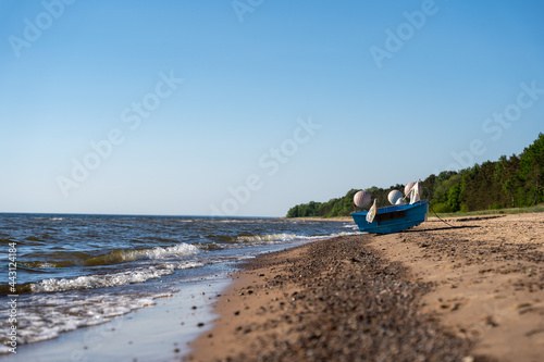 Baltic Sea beach with clear skies and green trees on the shore, but a small fishing boat stands by the water's edge