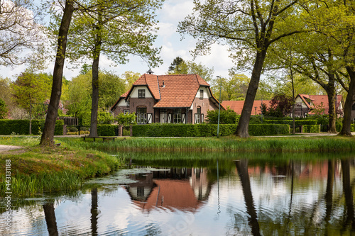 Dutch authentic house near the river with reflections in the water, surrounded by trees and greenery on a sunny day during spring in Grientsveen, The Netherlands