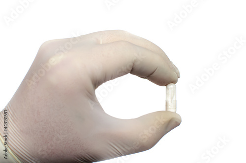 A man's hand in a latex glove holds the capsule isolated on white