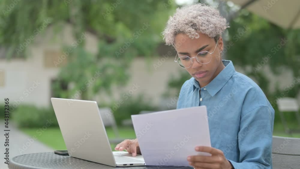 Young African Woman with Laptop Reading Documents in Outdoor Cafe Young African Woman with Laptop Reading Documents in Outdoor Cafe