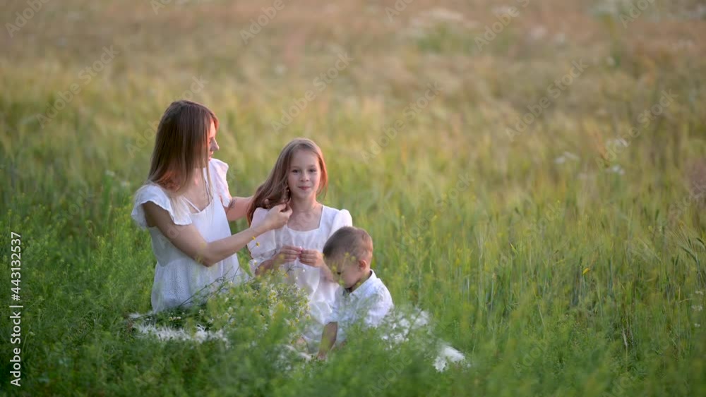 Happy young mom plays with children while sitting on green grass in the field. Happy family outdoors. Holiday and lifestyle concept. Happy young mom plays with children while sitting on green grass in the field. Happy family outdoors. Holiday and lifestyle concept.